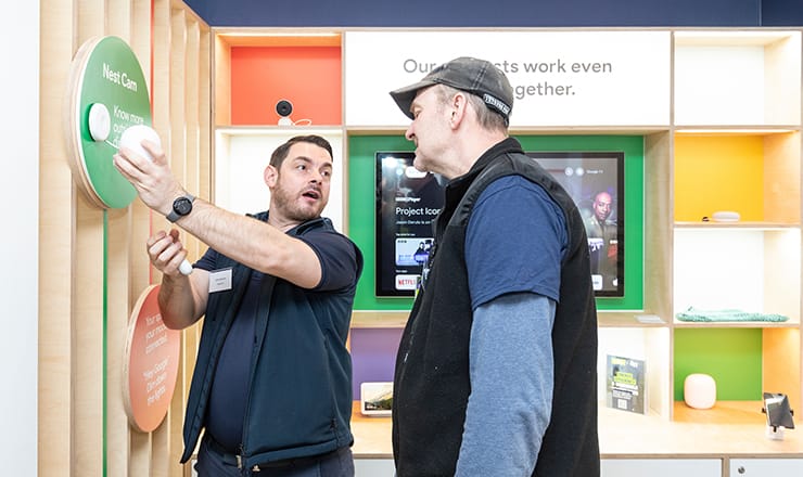Two men stand by a wall at an energy efficiency centre. One is pointing something out while the other looks on