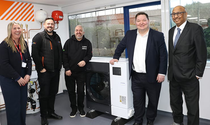 Line-up of 5 people standing around a Mitsubishi Electric heat pump in a training centre, two of whom are Andrew Western, MP for Stretford and Urmston, and Sir Mark Hendrick, MP for Preston