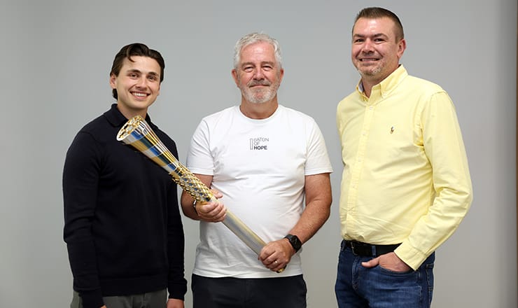 3 representatives from Oxford United Football Club, Baton of Hope charity, and Baxi, holding a torch, signifying their collaboration to work together to prevent suicide