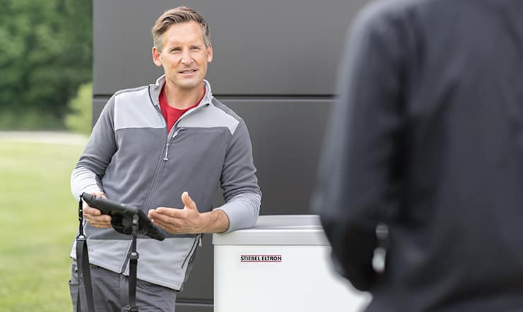 A mid-age white man leans on a Stiebel Eltron heat pump, holding an electronic tablet