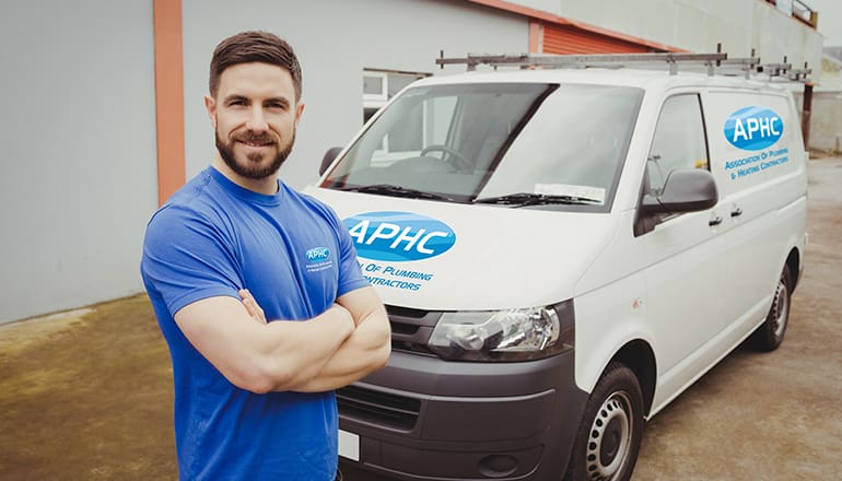 A man in a blue T shirt standing by his white van, which has carries a logo for the APHC
